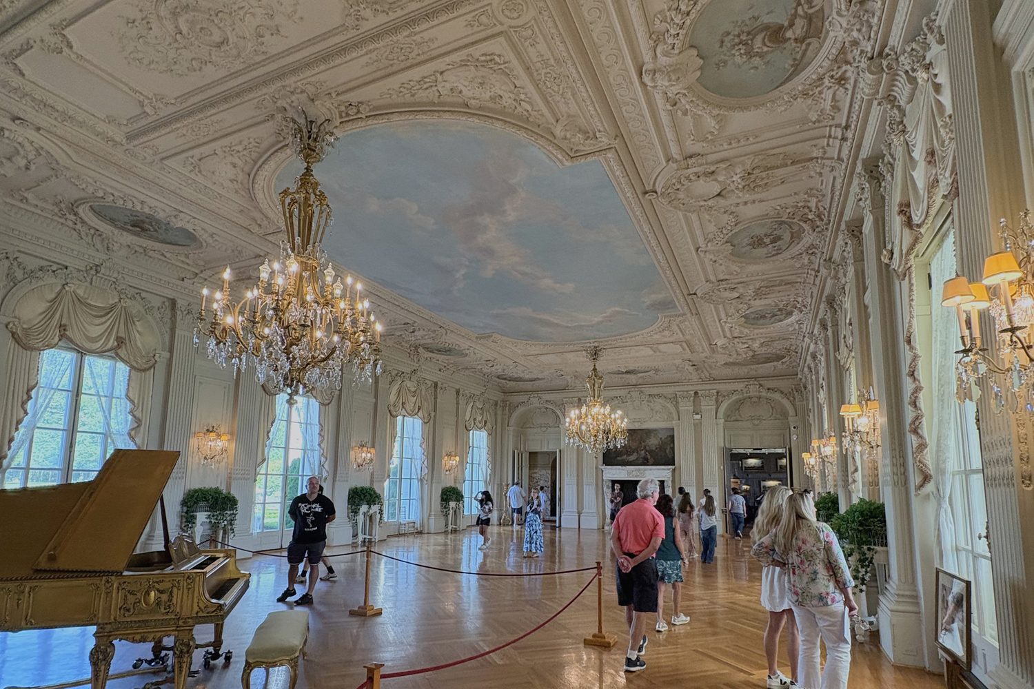 A long parquet gallery under a painted ceiling, piano at the far end