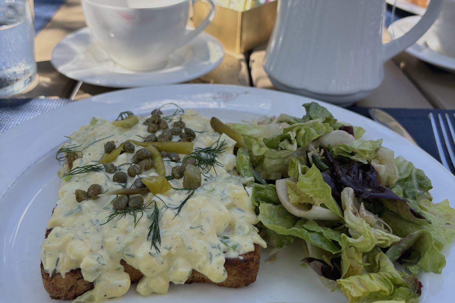Breakfast laid on a terrace table with a white teapot and cup