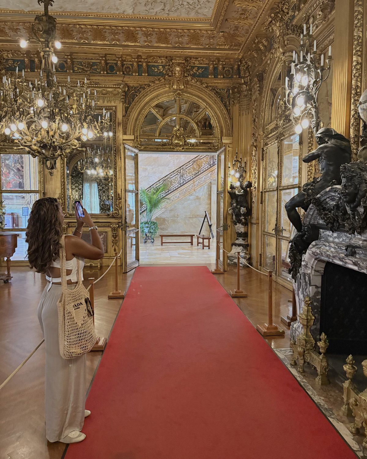 A figure walking a red-carpeted enfilade between gilt rooms